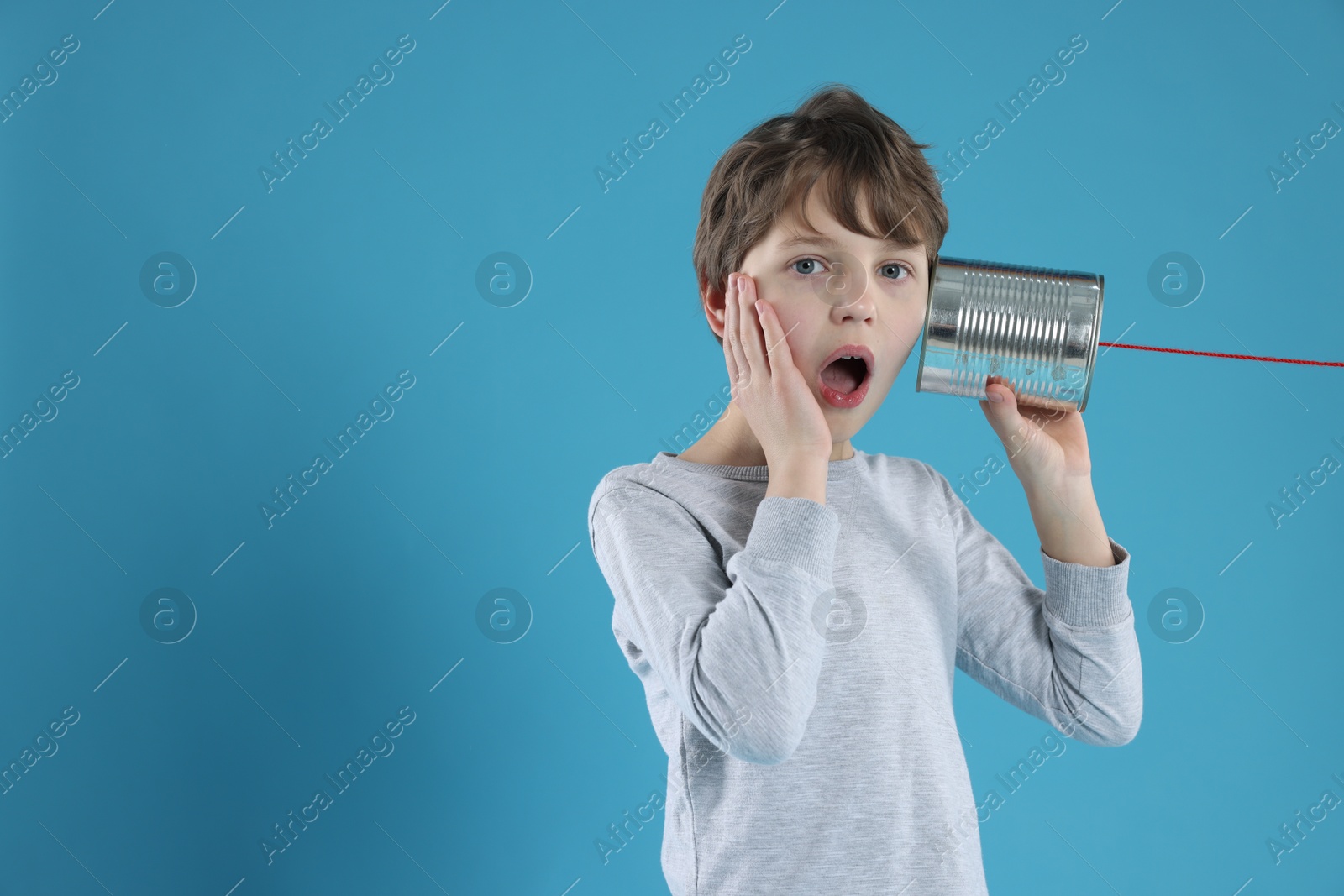 Photo of Surprised boy using tin can telephone on blue background. Space for text