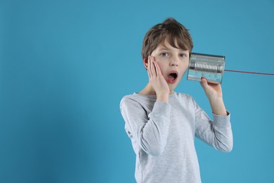 Photo of Surprised boy using tin can telephone on blue background. Space for text