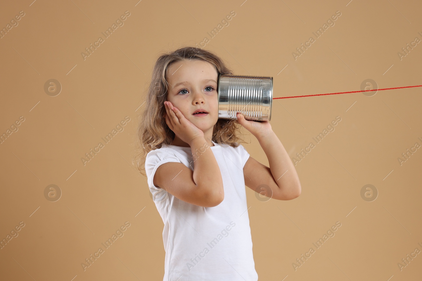 Photo of Girl using tin can telephone on beige background