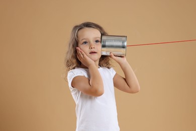 Photo of Girl using tin can telephone on beige background