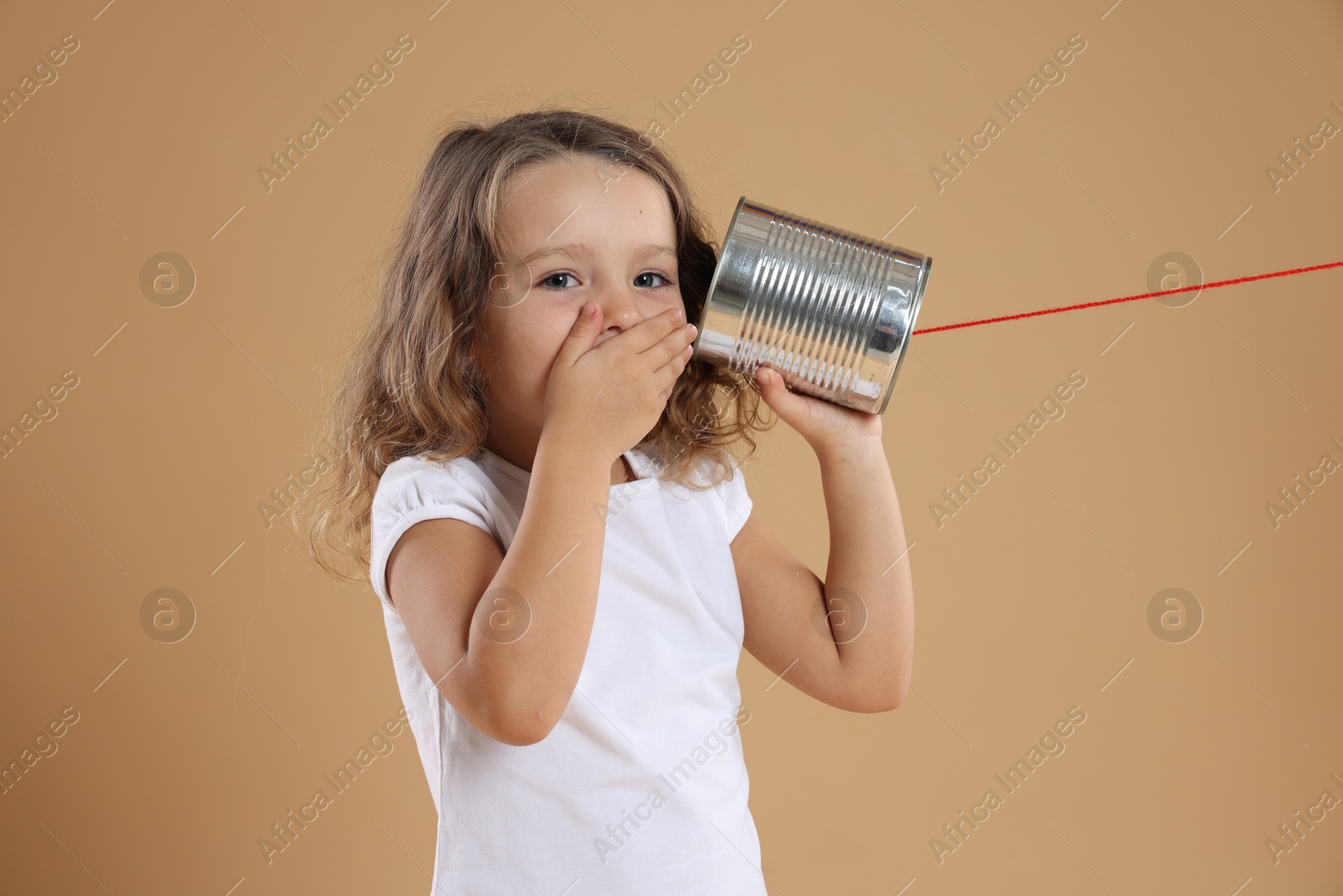 Photo of Excited girl using tin can telephone on beige background