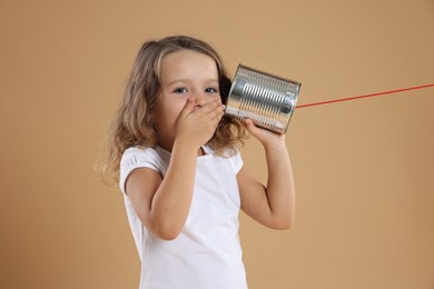 Photo of Excited girl using tin can telephone on beige background