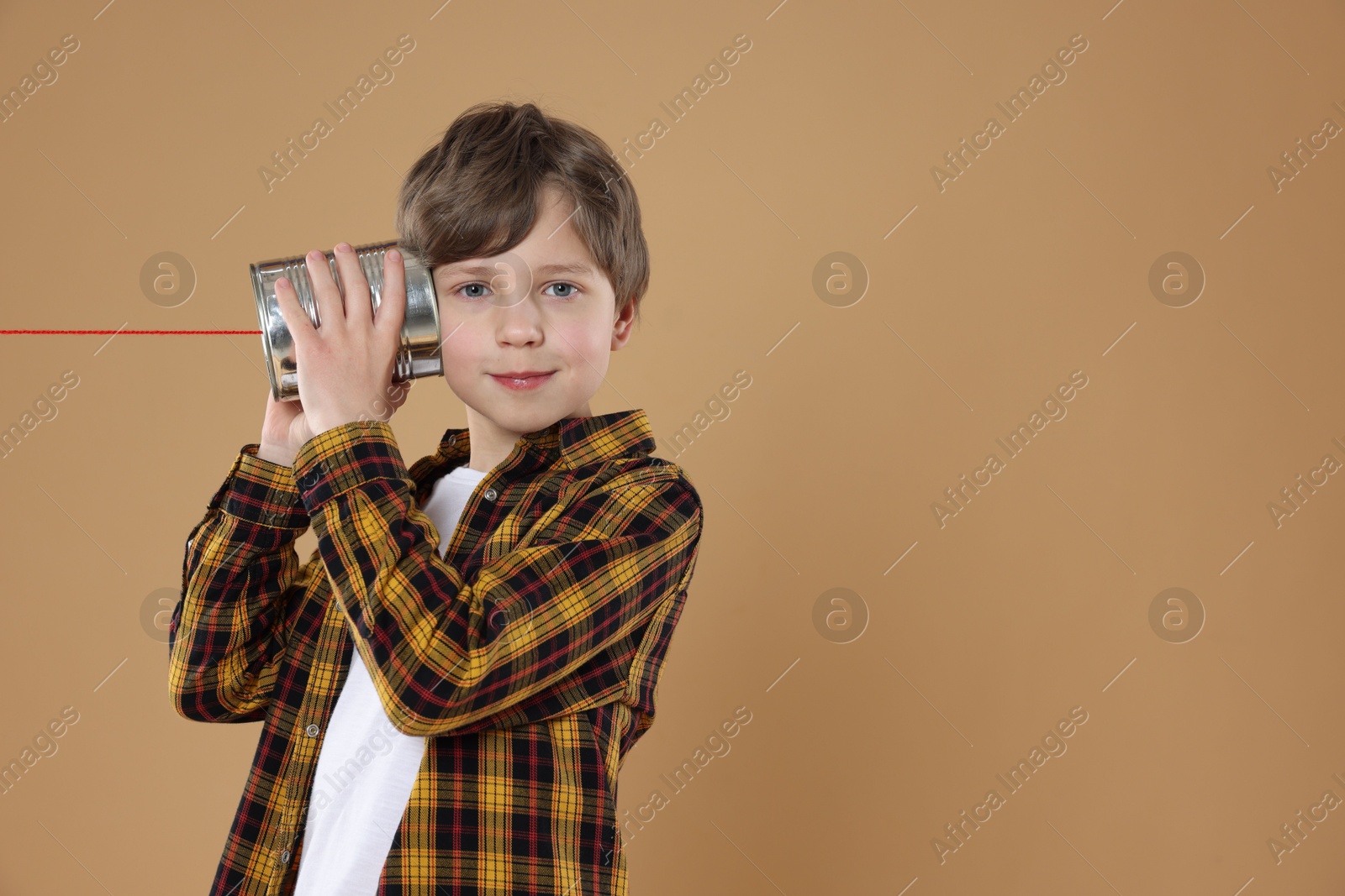 Photo of Boy using tin can telephone on beige background. Space for text