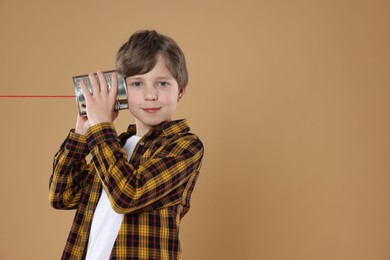 Photo of Boy using tin can telephone on beige background. Space for text