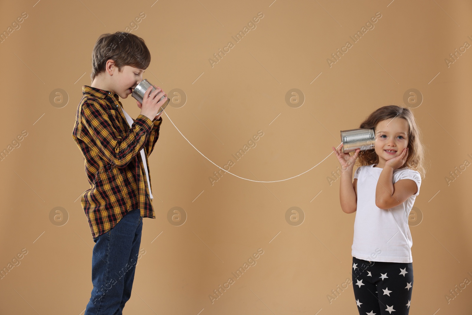 Photo of Boy and girl talking on tin can telephone against beige background