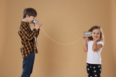 Photo of Boy and girl talking on tin can telephone against beige background