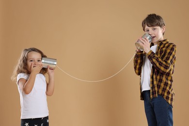 Photo of Boy and girl talking on tin can telephone against beige background