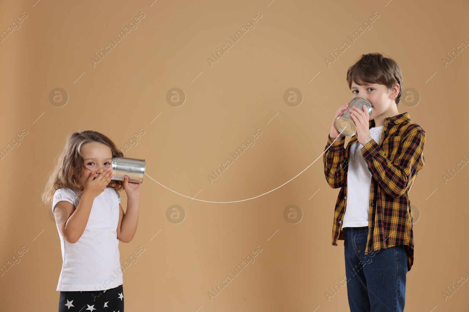 Photo of Boy and girl talking on tin can telephone against beige background