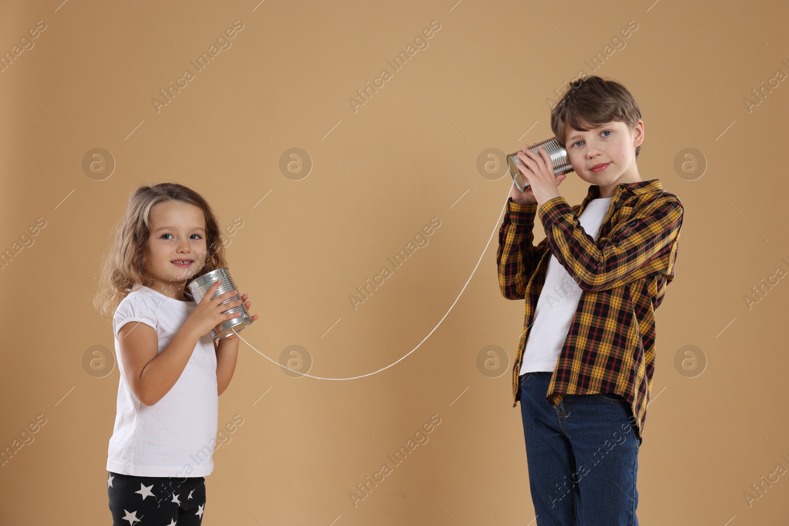 Photo of Boy and girl talking on tin can telephone against beige background