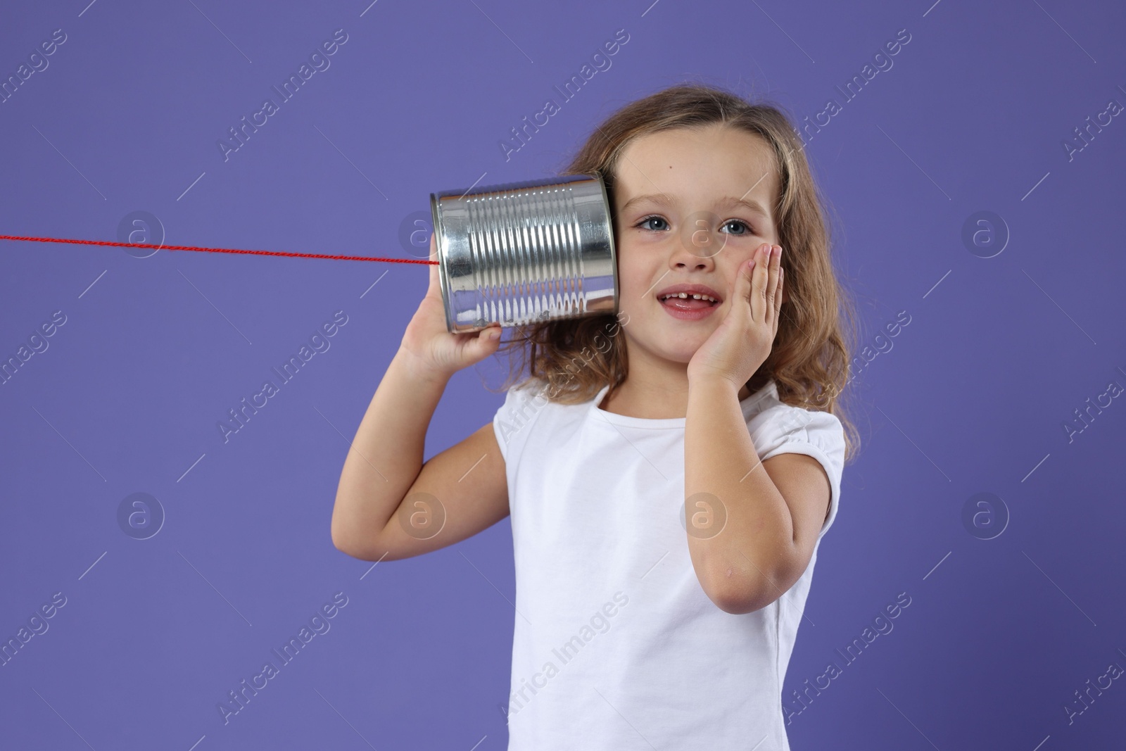 Photo of Excited girl using tin can telephone on violet background