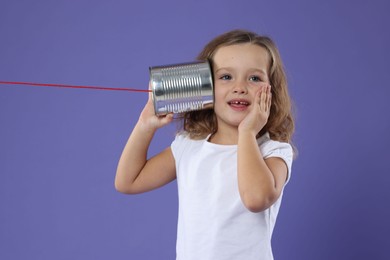 Photo of Excited girl using tin can telephone on violet background