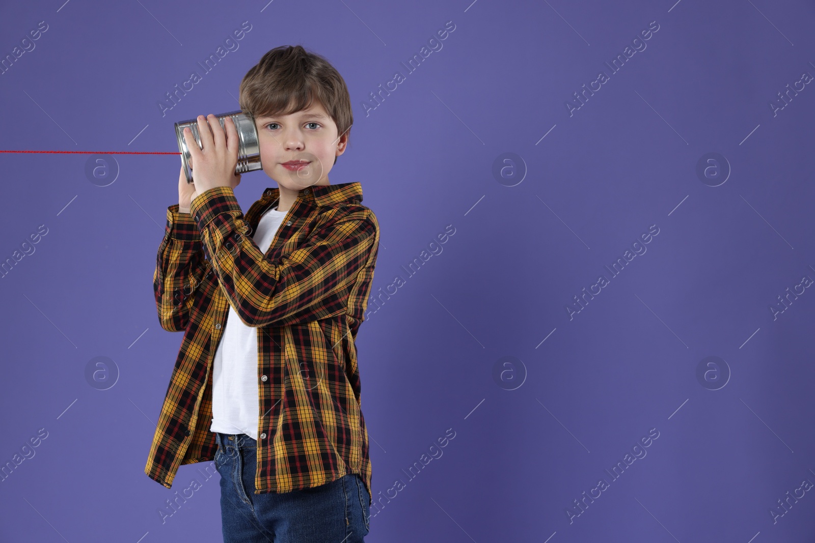 Photo of Boy using tin can telephone on violet background. Space for text