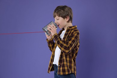 Photo of Boy using tin can telephone on violet background