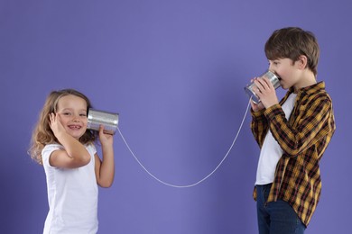 Photo of Boy and girl talking on tin can telephone against violet background