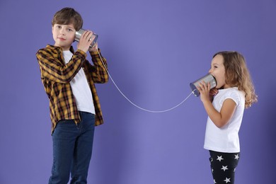 Photo of Boy and girl talking on tin can telephone against violet background