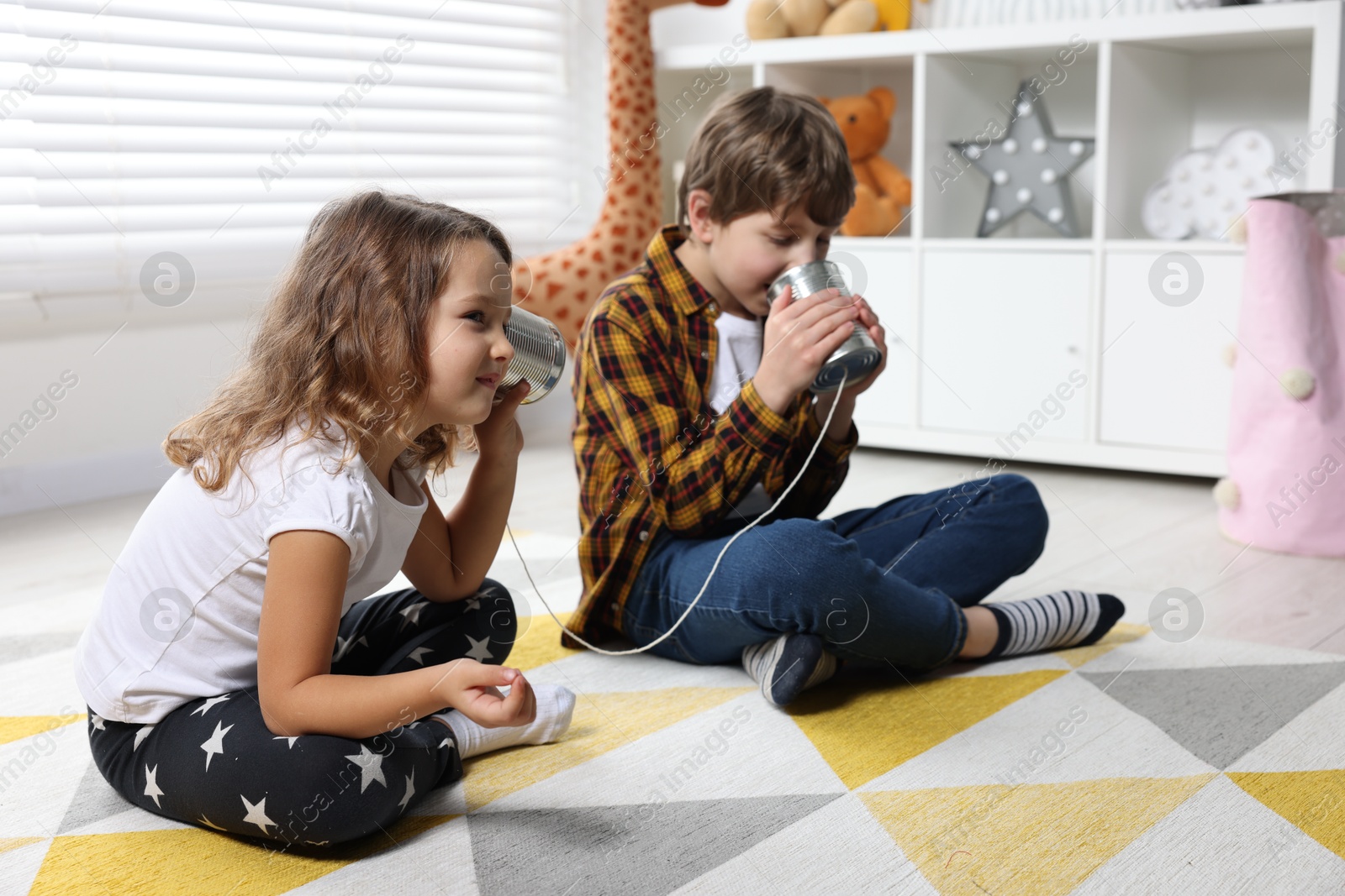 Photo of Boy and girl talking on tin can telephone indoors