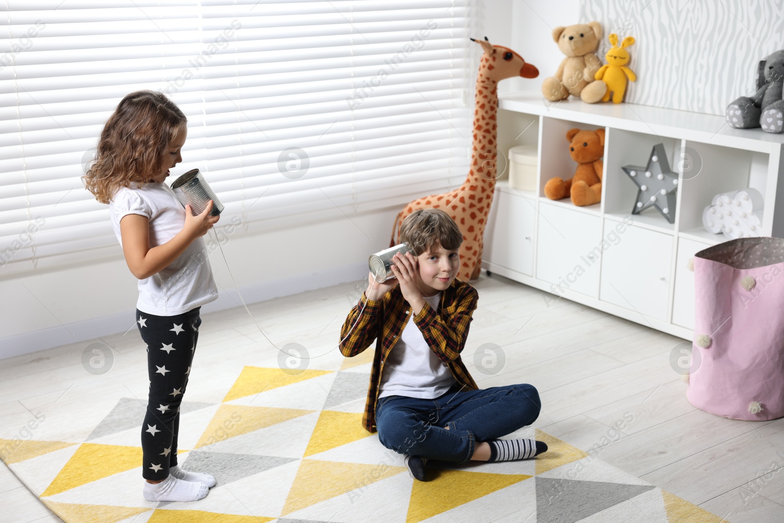 Photo of Boy and girl talking on tin can telephone indoors