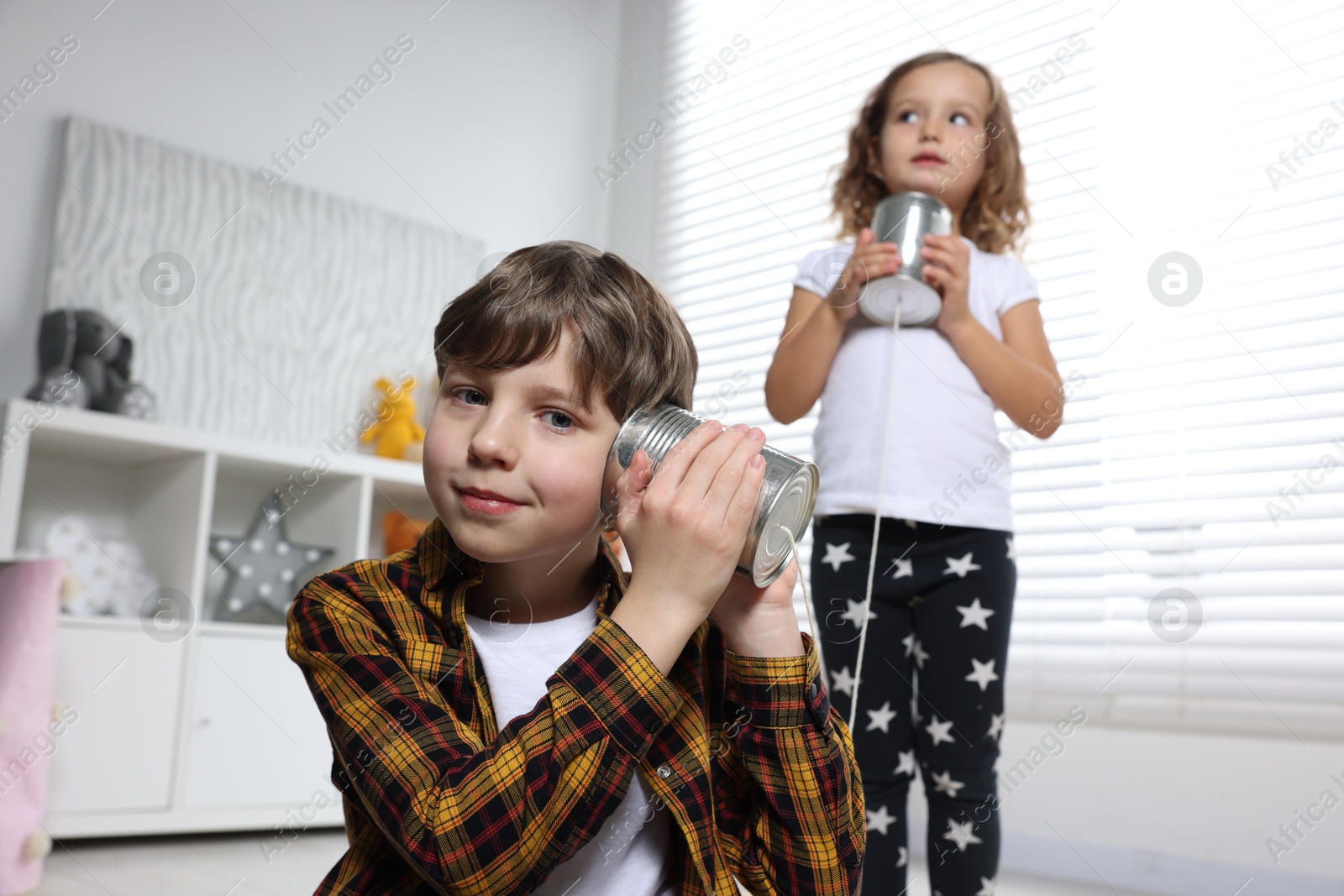 Photo of Boy and girl talking on tin can telephone indoors, selective focus