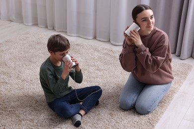 Photo of Woman and boy talking on tin can telephone indoors