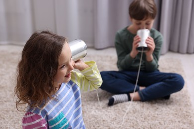 Photo of Boy and girl talking on tin can telephone indoors, selective focus