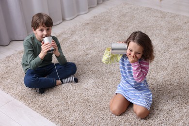 Photo of Boy and girl talking on tin can telephone indoors