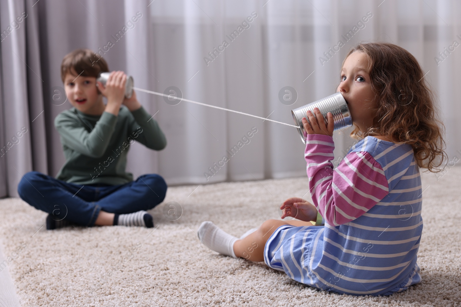 Photo of Boy and girl talking on tin can telephone indoors, selective focus