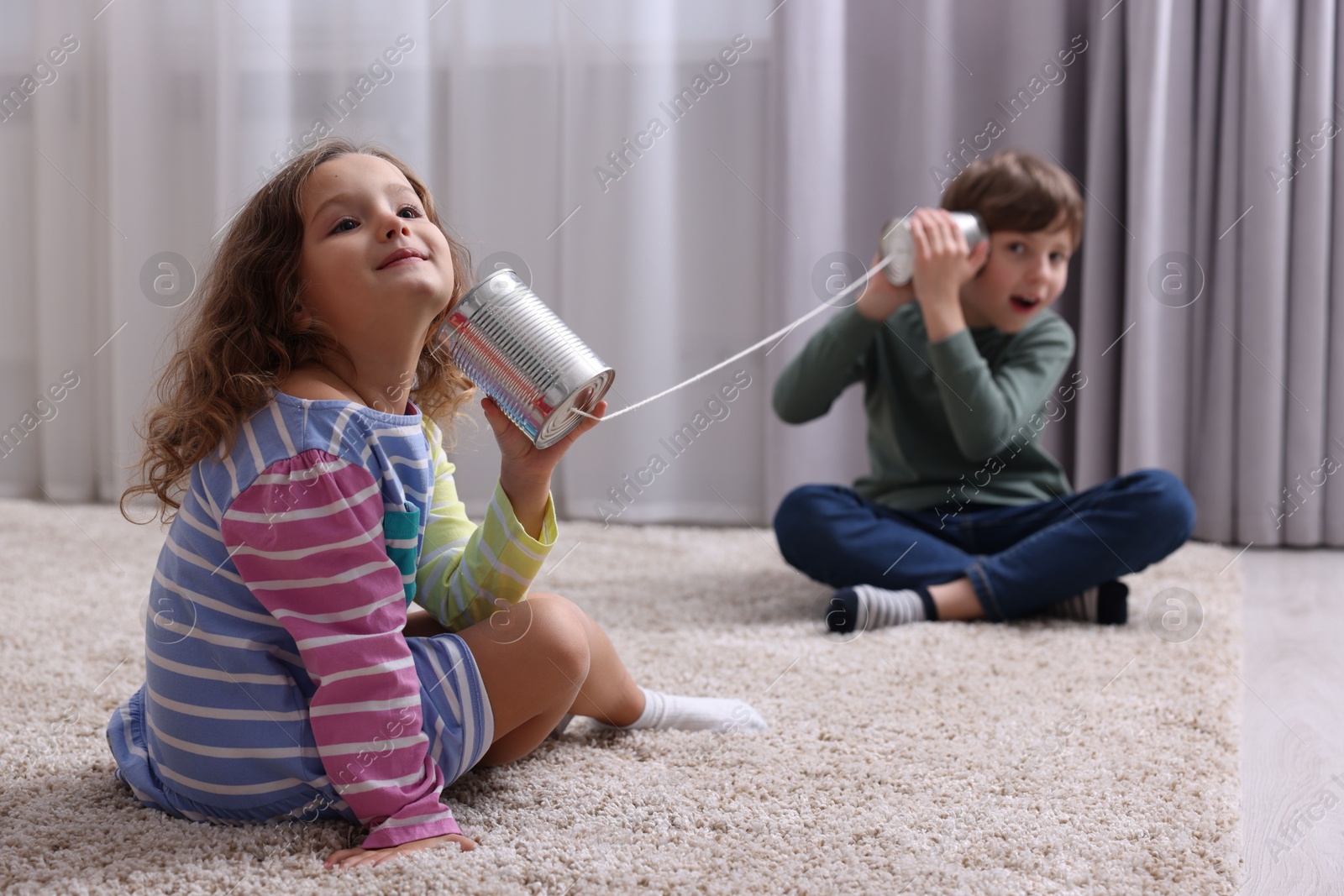 Photo of Boy and girl talking on tin can telephone indoors, selective focus