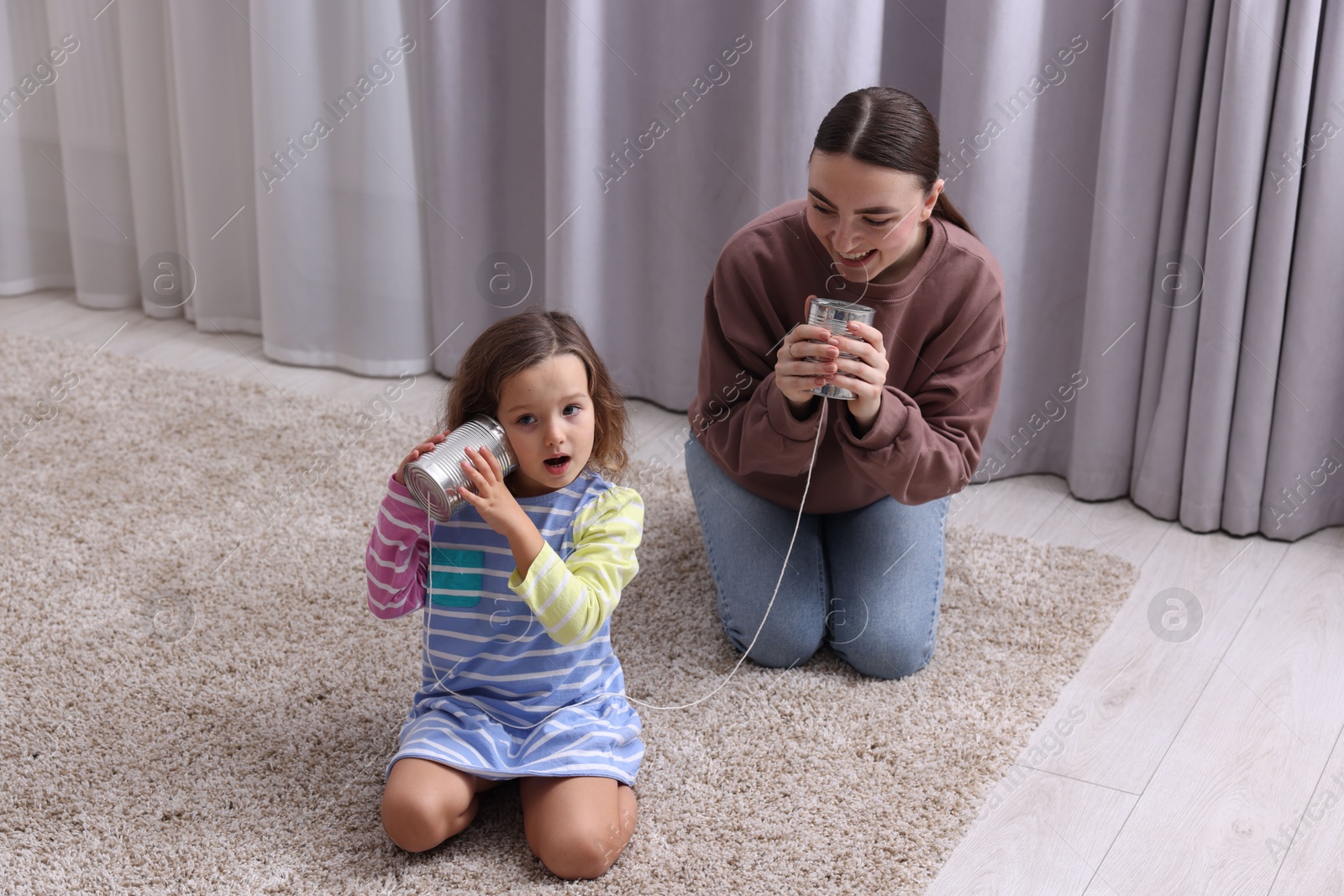 Photo of Woman and girl talking on tin can telephone indoors