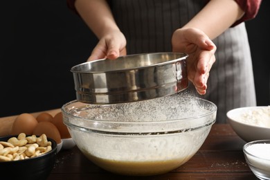 Photo of Making cashew cookies. Woman sieving flour into dough at wooden table, closeup