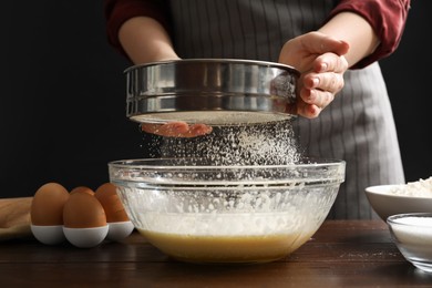 Photo of Making cookies. Woman sieving flour into dough at wooden table, closeup