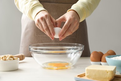 Photo of Making cashew cookies. Woman adding egg into bowl at white wooden table, closeup