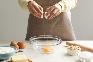 Photo of Making cashew cookies. Woman adding egg into bowl at white wooden table, closeup