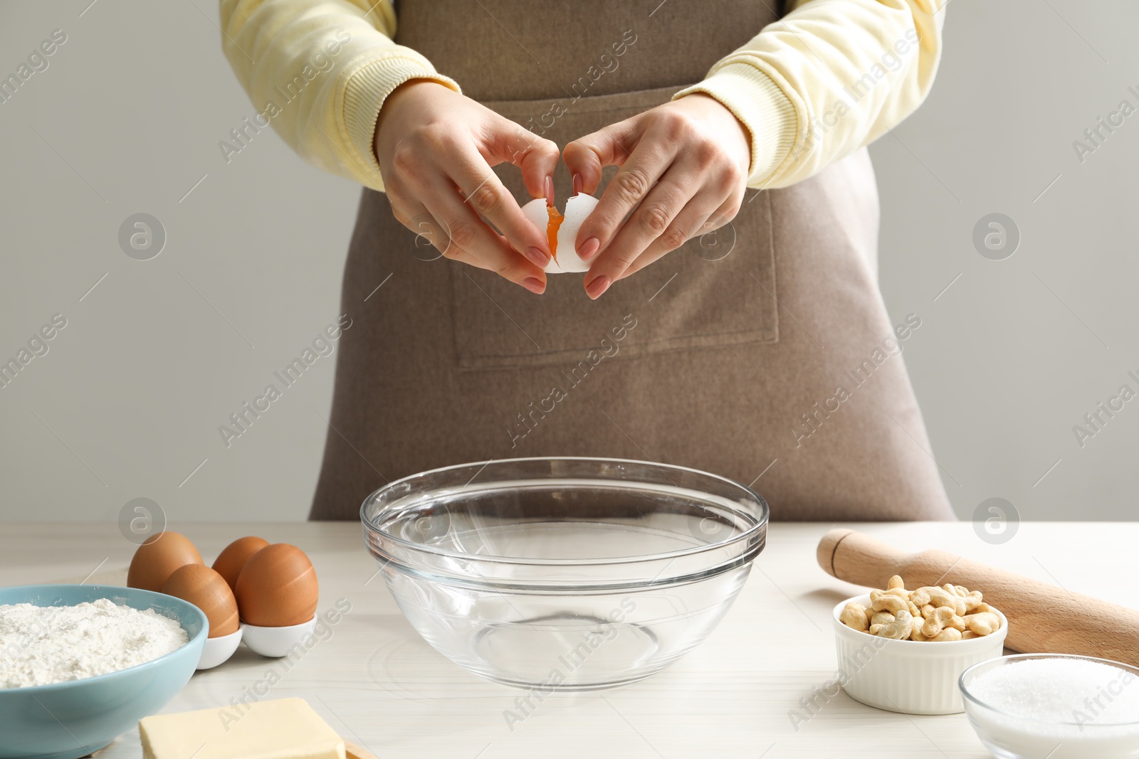 Photo of Making cashew cookies. Woman adding egg into bowl at white wooden table, closeup