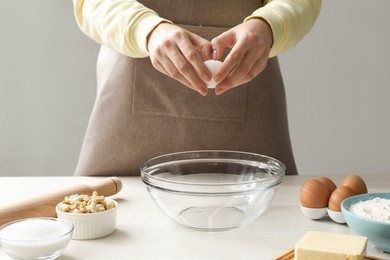 Photo of Making cashew cookies. Woman adding egg into bowl at white wooden table, closeup