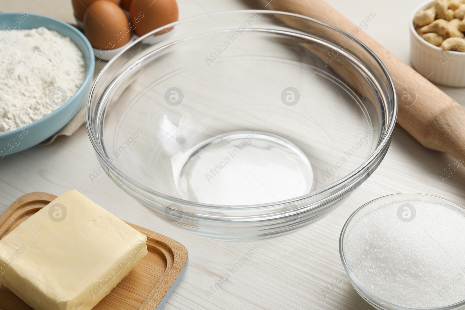 Photo of Bowl and ingredients for cookies on white wooden table, closeup