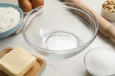 Photo of Bowl and ingredients for cookies on white wooden table, closeup