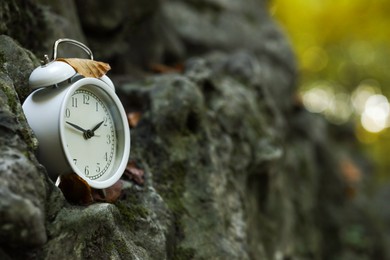 Photo of Alarm clock on stones outdoors, closeup. Space for text