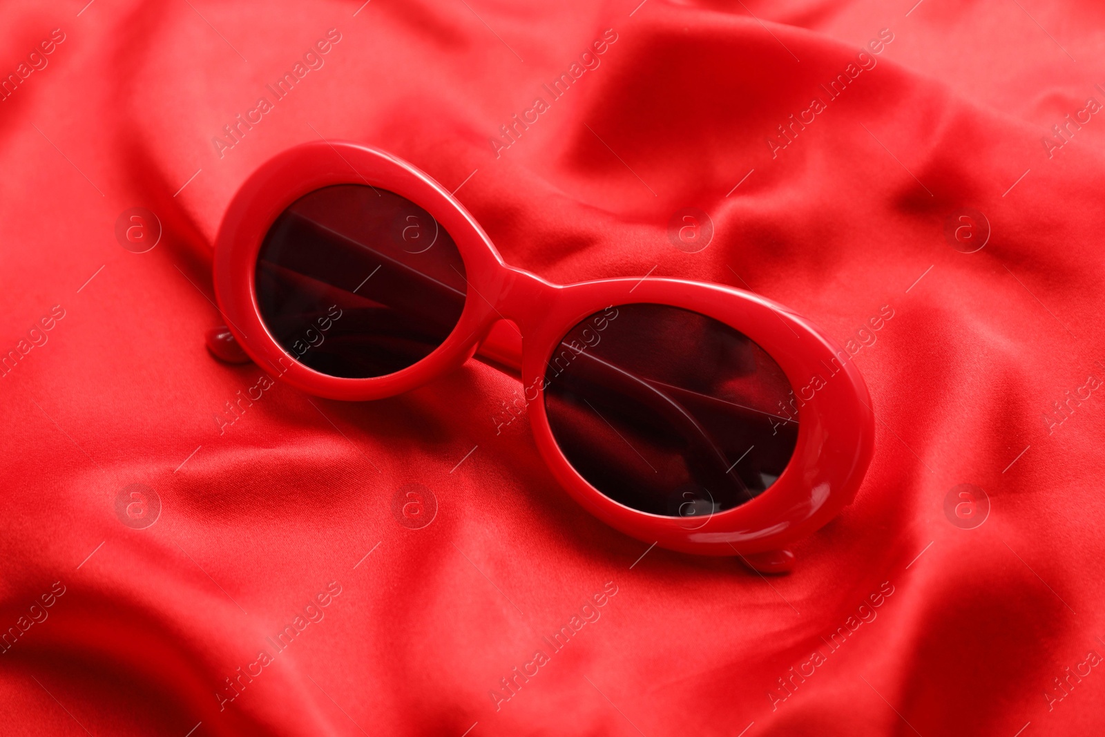 Photo of Stylish sunglasses on red fabric. Elegant accessory