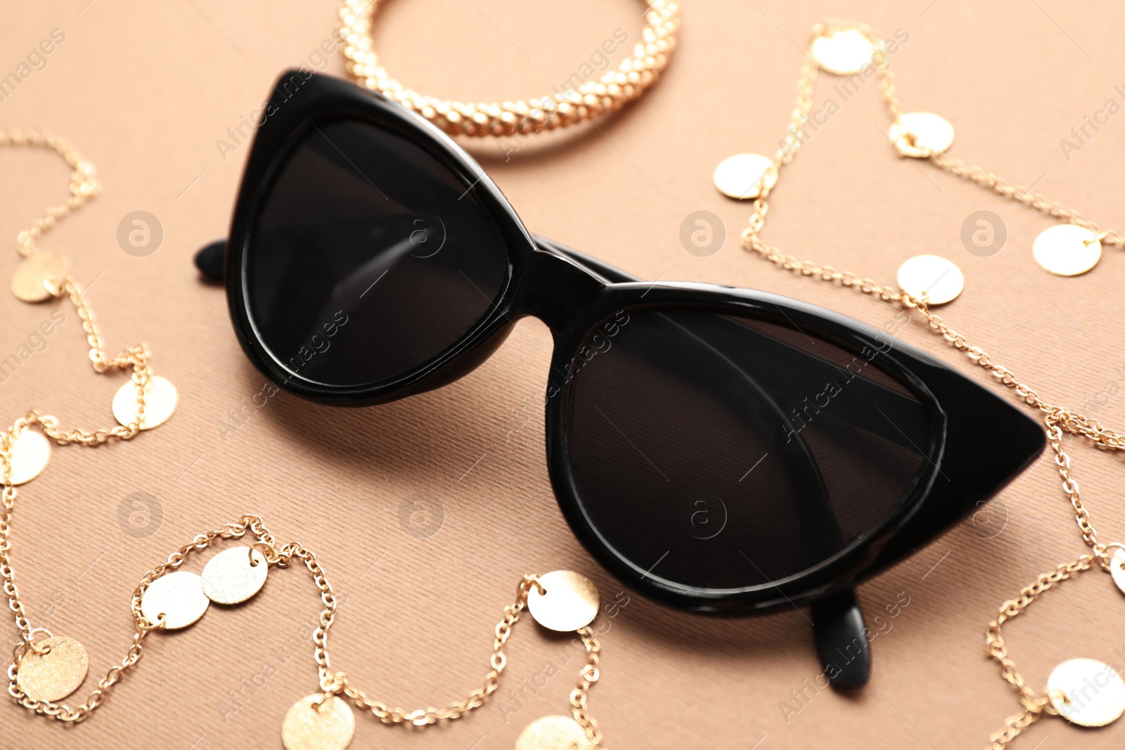 Photo of Stylish sunglasses and jewelry on beige background, closeup. Elegant accessory