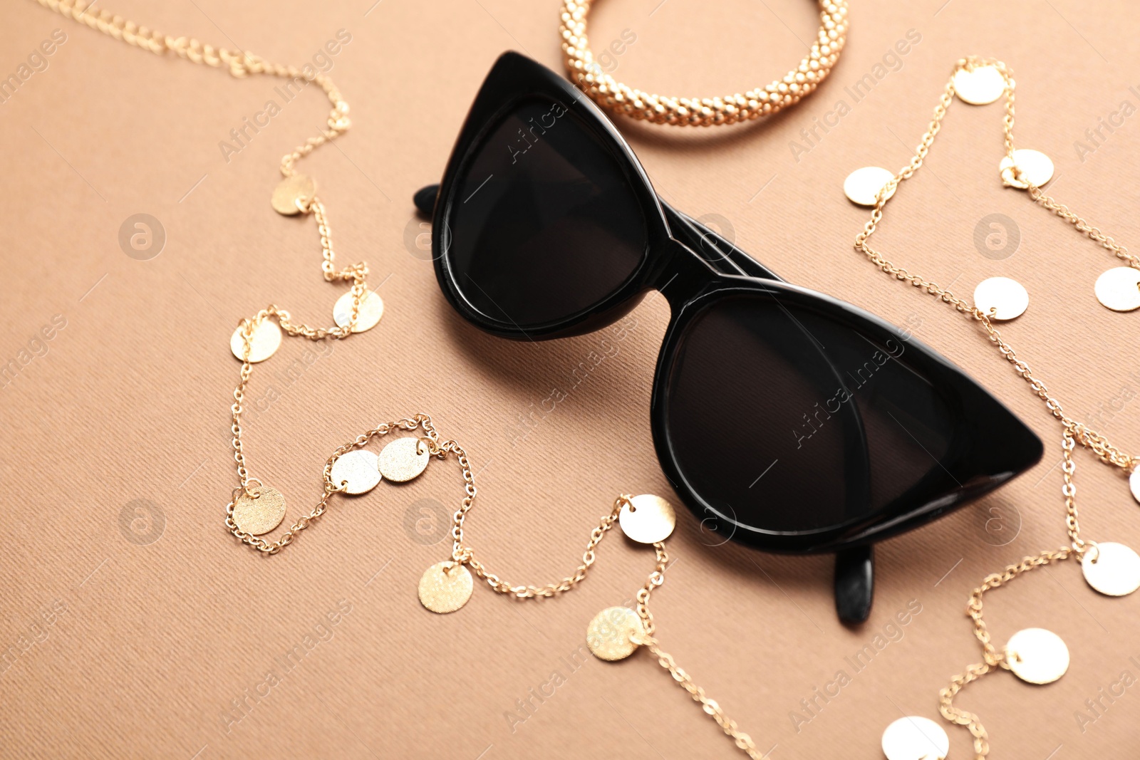 Photo of Stylish sunglasses and jewelry on beige background. Elegant accessory