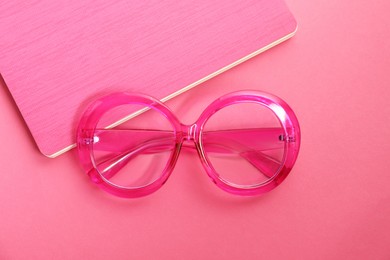 Photo of Stylish bright glasses and notebook on pink background, top view