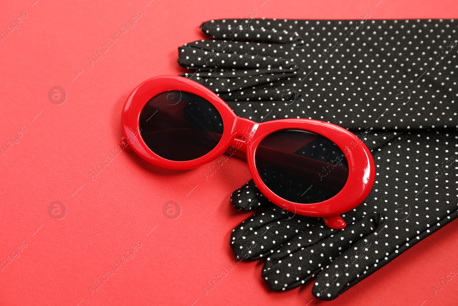 Photo of Stylish sunglasses and polka dot gloves on red background. Elegant accessory