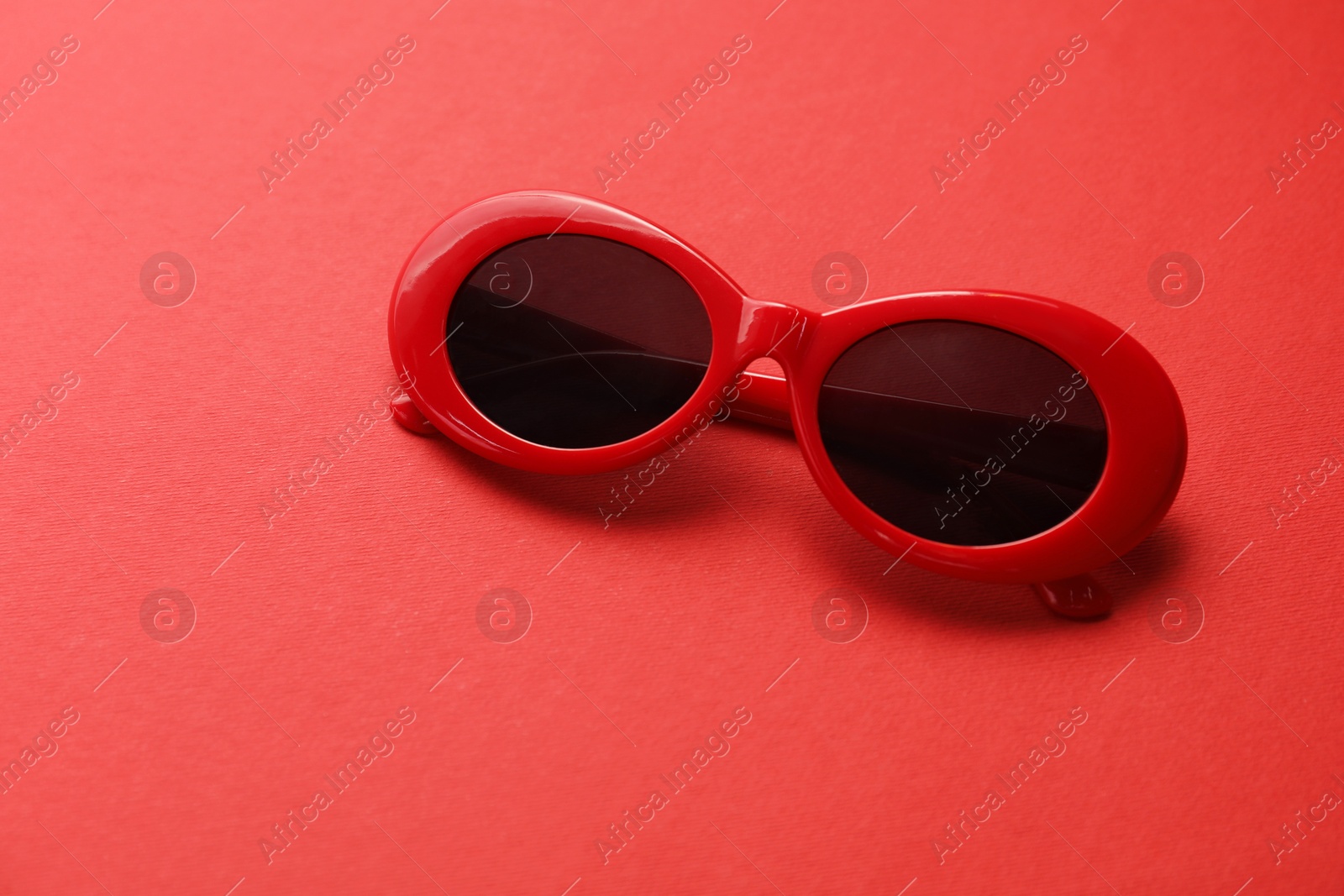 Photo of Stylish sunglasses on red background. Elegant accessory