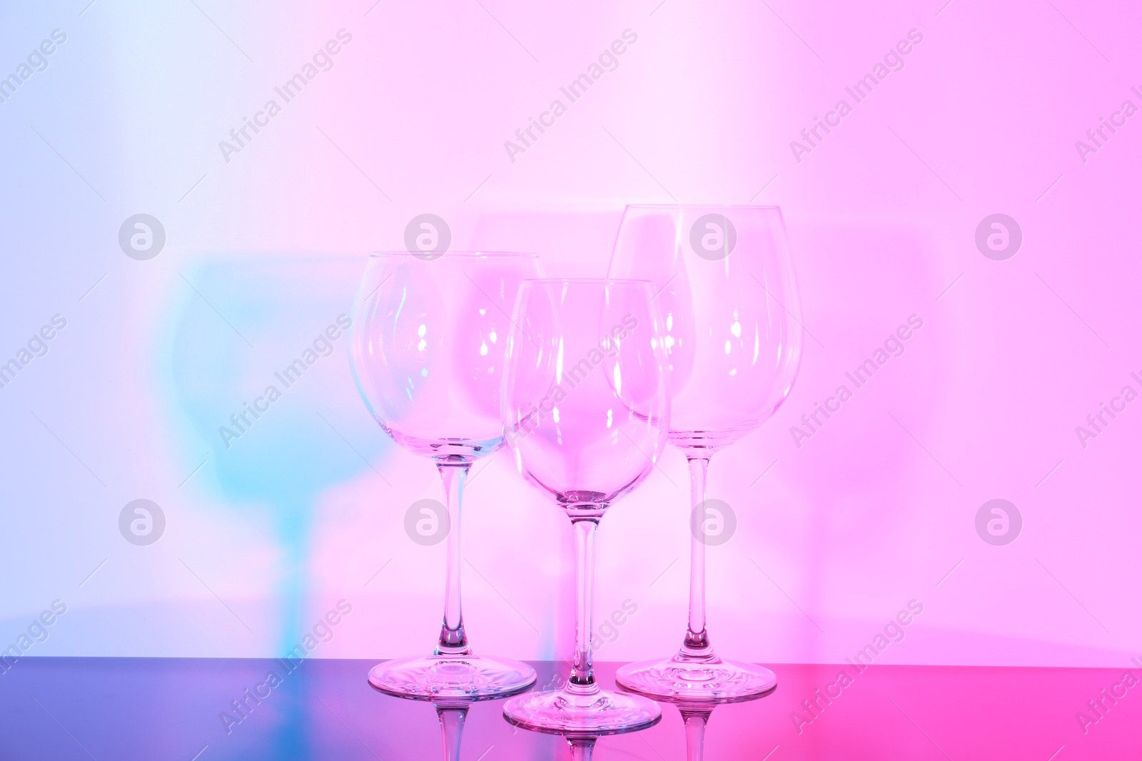 Photo of Empty glasses on table against color background