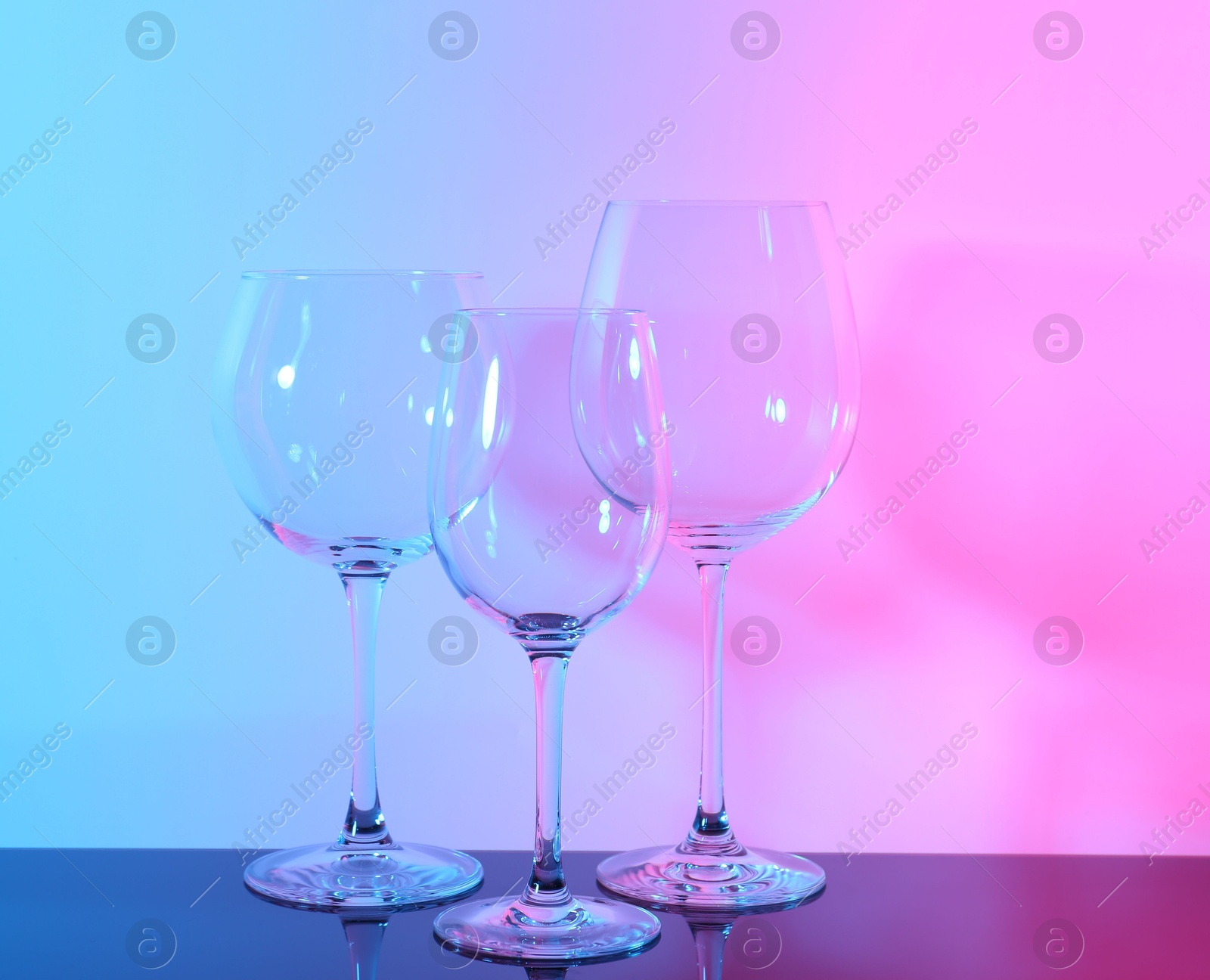 Photo of Empty glasses on table against color background