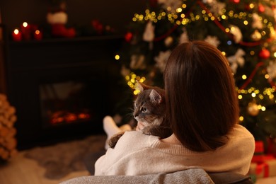 Photo of Woman with cute cat in room decorated for Christmas, back view. Space for text