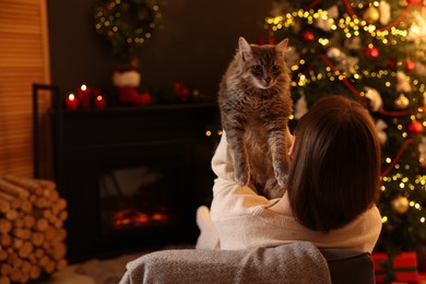 Photo of Woman with cute cat in room decorated for Christmas, back view. Space for text