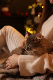 Woman with cute cat against blurred Christmas lights, closeup