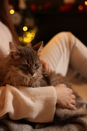 Photo of Woman with cute cat against blurred Christmas lights, closeup