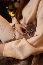 Photo of Woman with cute cat against blurred Christmas lights, closeup